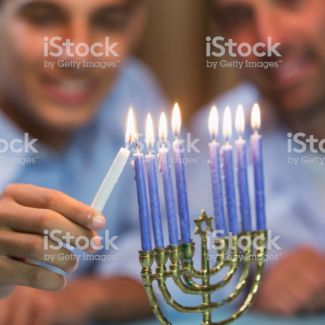 A father and his teenage son celebrating hanukkah, lighting the menorah. The focus is on the menorah in the foreground.